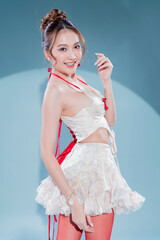 Elegant Asian model in white lace corset top and ruffled mini skirt with red ribbon accents, posing confidently in sheer red stockings and nude high heels, glamorous studio portrait soft blue scene