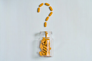 Orange supplements arranged in a distinct question mark shape above an open clear medication bottle.