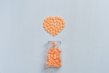 Bright orange circular medication tablets artistically arranged in a heart shape above an open prescription bottle.