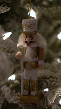 Christmas ornaments hang on snowy pine tree with nutcracker toy standing out. Warm lights create cozy atmosphere. Perfect for showcasing holiday decorations and winter charm.