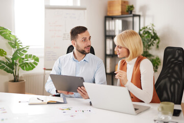 Obraz premium Two team members collaborate and share ideas while working on a tablet during a meeting at an office. They focus on improving their business strategies and teamwork.