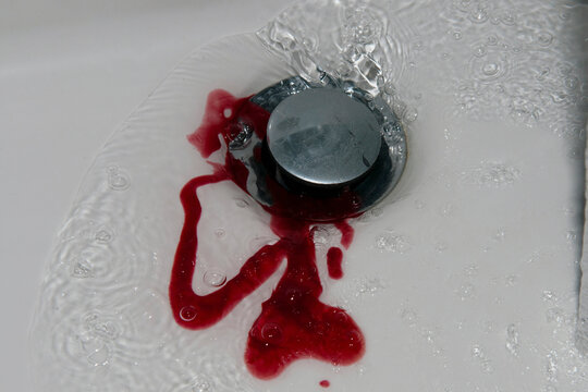 Blood in water swirling down basin drain in a studio setting