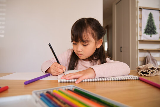 Child drawing with colored pencils at home focused on artwork