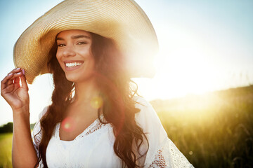 Fototapeta premium Portrait, woman and happy for travel outdoor with peace, fresh air and calm morning on holiday. Lens flare, female person and vacation with straw hat in field, weekend break and summer in countryside