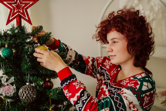 Person decorating Christmas tree in pyjama at home during winter holiday