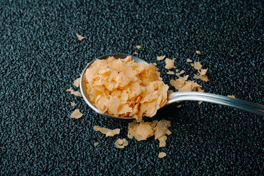 Nutritional yeast flakes spilling from metal spoon on black textured surface