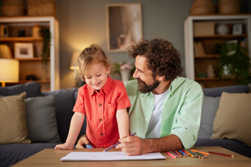Obraz premium A father and daughter share joyful moments as they create art together at home. They use colorful pencils while seated at a simple table in a warm, welcoming environment.