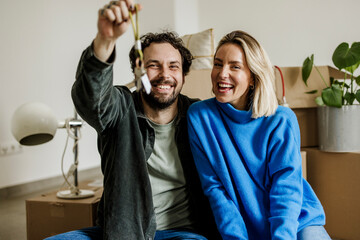 Happy couple sitting indoors with keys celebrating new home ownership
