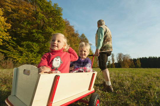 Child and family member pulling wagon through autumn field outdoors