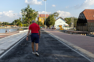Rear view of an elderly man wearing a red shirt walking for exercise in a city park. Concept of healthy lifestyle, aging well, outdoor fitness, and active senior life in an urban environment.