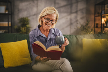 Mature woman sit in the living room read a book and drink coffee