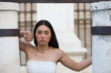 A young, attractive Spanish woman dressed in a white lace top, black shorts and leather boots strikes various poses between two stone columns next to Seville Cathedral.