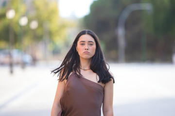 A young, attractive Spanish woman wearing a brown dress walks like a model down a street in Seville, Spain. The woman strikes a pose as she walks. Concept: beauty and fashion.