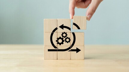 A human hand carefully positions the final wooden block to complete a cycle diagram featuring gears symbolizing system development efficiency and continuous improvement o