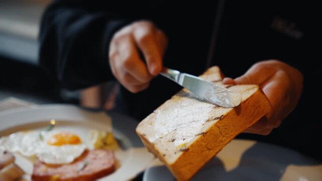 Person spreading butter on grilled toast during breakfast
