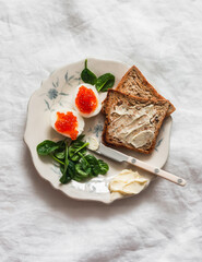 Delicious breakfast, brunch, tapas, snack - boiled eggs with red caviar, toasts with butter, spinach on a light background, top view
