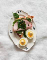 Delicious grilled breakfast - bread toast with cream cheese, spinach, ham, pumpkin seeds, boiled egg on a light background, top view
