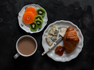 Breakfast served, brunch on a dark background, top view. Croissant, coffee, cheese, fruit - a delicious start to the day