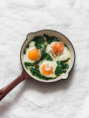 Fried eggs with spinach in a cast-iron skillet on a light background, top view