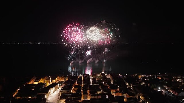 Aerial view of Lazise, Lake Garda, Italy, during fireworks on August 24, 2025. Drone footage captures the historic center, lakeside town, evening lights, and summer celebration in 4K.