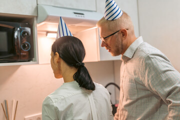 Here's a title following your specifications: **Couple Birthday Party Kitchen Microwave Celebration: Man and woman wearing party hats prepare food in office kitchen during birthday celebration.**