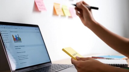A professional brainstorming and organizing ideas with colorful sticky notes on a wall and a laptop for digital planning, demonstrating collaboration in a modern workspace.