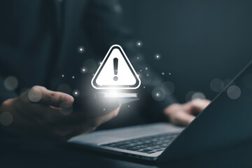Glowing warning alert icon floating above smartphone and laptop, representing cybersecurity threat, system error, digital risk notification, data protection issue, online security technology concept.