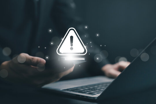 Glowing warning alert icon floating above smartphone and laptop, representing cybersecurity threat, system error, digital risk notification, data protection issue, online security technology concept. - Powered by Adobe