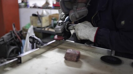 Metalworker in respirator mask and gloves grinding a steel surface with an angle grinder, focused on precise metal fabrication and safety in an industrial workshop setting