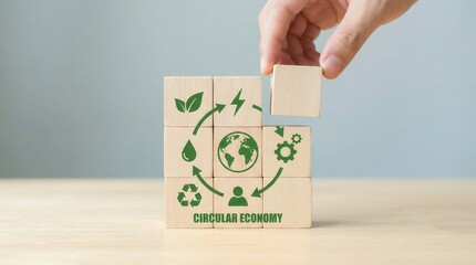 A human hand carefully places a wooden block to complete an arrangement illustrating the circular economy concept with green icons against a soft light background