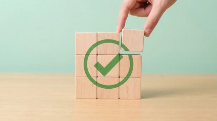 A human hand carefully places a wooden block with a vibrant green checkmark symbol into a grid of blocks on a smooth wooden table against a soft pastel green background d