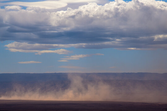 View of a dust devil dances across the arid landscape under a vast sky of dramatic clouds, casting long shadows on the ground, Page, Arizona, United States.