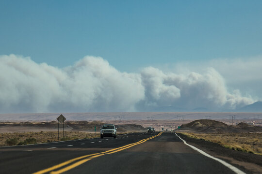 View of black asphalt road stretching into the horizon under a pale blue sky, with a massive dust storm looming over the arid landscape, Page, Arizona, United States.