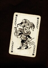 A vintage joker playing card in sepia isolated on a black background.