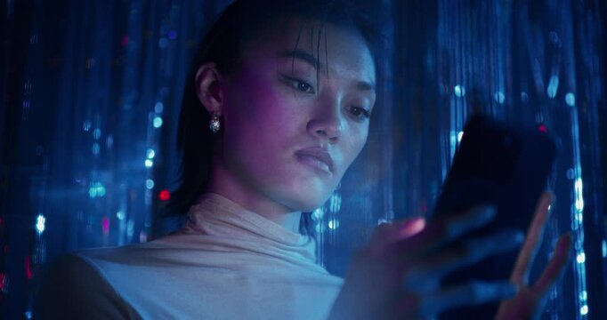 A woman uses a mobile phone with a serious look standing among sparkling blue tinsel
