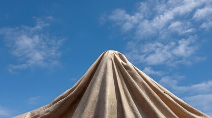 Textured beige fabric draped over a structure against a bright blue sky with scattered clouds