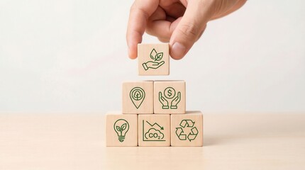Human hand places wooden block with green leaf and water icon completing a pyramid of environmental symbols on bright light table with soft lighting illustrating clean fu