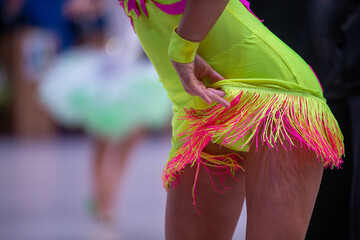 Close-up female latin dancer in bright neon yellow dress with pink fringe
