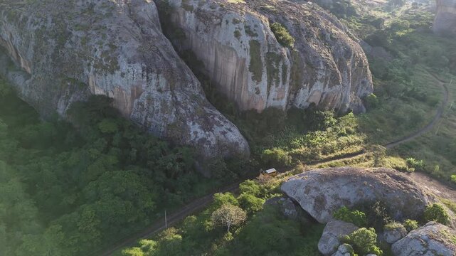 Cinematic drone flyover of volcanic stone monoliths at Pedras Negras, Angola while a camper van truck overloading driving narrowed path