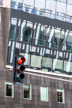 Urban city street with traffic light reflected in glass building facade showing modern architecture and busy commute atmosphere at intersection