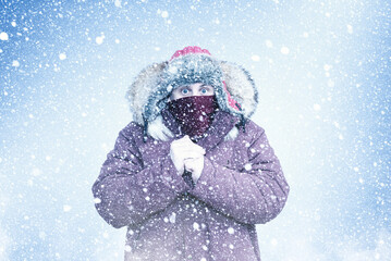 Man in warm winter clothing warming his hands during heavy snowfall. Cold weather concept, freezing temperatures, winter storm, frost, survival, extreme cold, seasonal climate background.