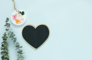 Flat lay of a black heart shaped chalkboard over a pastel blue background, eucalyptus leaves and a scented wax sachet. Ideal top view for love, greeting cards, mother's day, valentines, concepts.