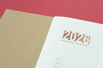 Close-up of an open planner showing the year "2026" and "Monthly Planner" on the first page, on a red background. Ideal for planning, new year, time management, business, and organizing concepts.