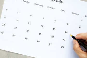 Person hand marking Valentine's Day on February 2026 calendar with pen, Planning romantic date or anniversary celebration, High angle view of calendar page with space for text.