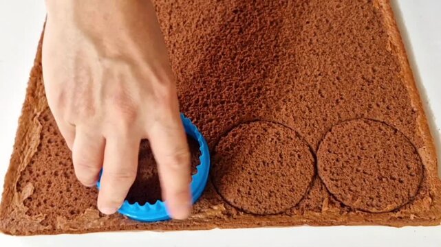 Cutting round circles from chocolate sponge cake sheet using a blue cookie cutter
