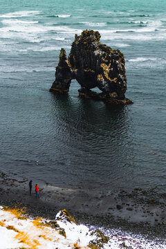 View of the monolithic rock formation of Hvitserkur rises majestically from the turbulent waters, as people observe the seascape, Blonduos, Vatnsnes peninsula, North Iceland, Iceland.
