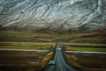 View of a lone car navigates the stark asphalt road cutting through the expansive Icelandic landscape with snowy mountains, Blonduos, Vatnsnes peninsula, North Iceland, Iceland.