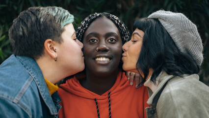 Two women kissing their friend while standing together outdoors