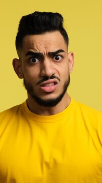 Vertical video of a young man looking shocked and disgusted. He shakes his head, crosses his arms, and shows a stop gesture, isolated on a yellow background.