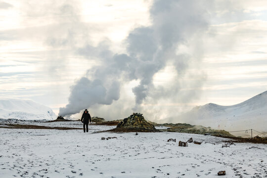 View of a lone figure amidst the geothermal vents and snowy landscape, with rising steam contrasting against the cold ground, Rejkjahlid, North Iceland, Iceland.